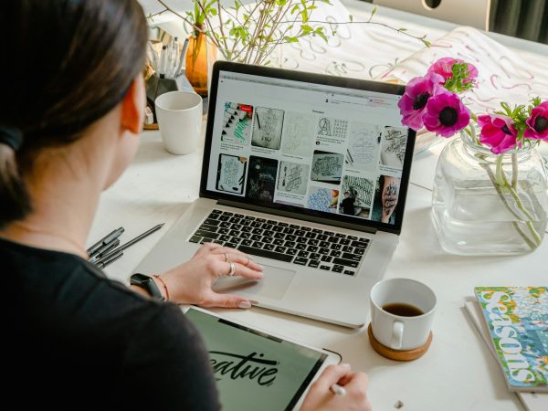 Woman in a creative workspace using a laptop and tablet for calligraphy. Artistic and tech-driven environment.