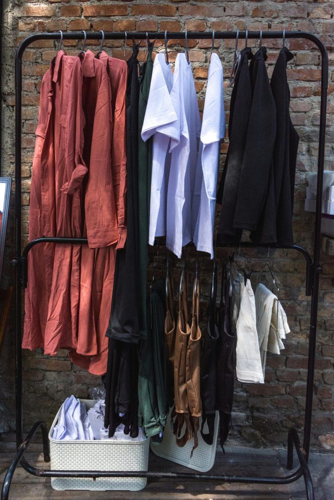 A diverse collection of garments neatly hung on a clothing rack against a rustic brick wall, showcasing fashion variety.