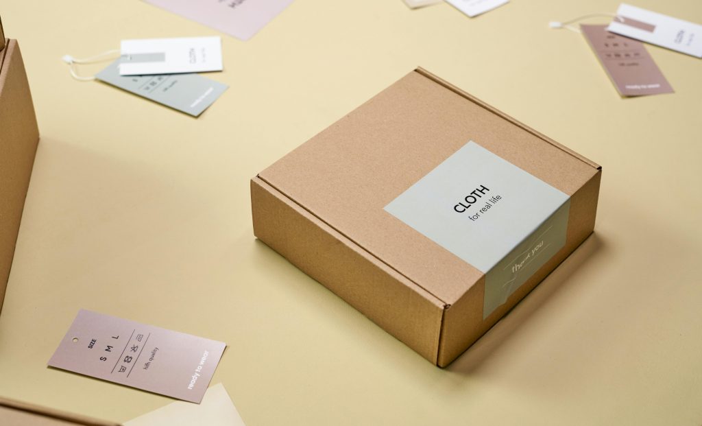 Elegant cardboard packaging with clothing labels and tags displayed on a light surface.